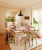 Bentwood chairs with cane seats and simple, rush-bottom chairs at festively set table in front of draped curtains