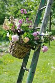 Colourful bouquet of garden flowers in basket hanging on ladder