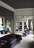 Doppelbett mit lila Tagesdecke, lila Polsterstuhl und weisser Einbauschrank mit Spiegeltüren in einem Schlafzimmer mit grauen Wänden