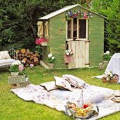 Idyllic picnic in garden with patchwork blanket and vintage fruit basket in front of shed decorated with flowers