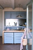 Youthful fitted kitchen with light blue fronts and stainless steel splashback; drawer units on castors below free-standing kitchen counter