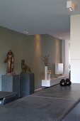 Theke mit grauer Steinplatte in offenem Wohnraum und Skulpturen auf Stele vor grau getönter Wand