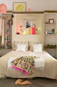Oriental dress on double bed against wall with illuminated niche in simple bedroom