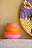 Stack of colourful plastic dishes and basketwork platter on stone shelf