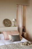 Bett mit Kissen neben luftigem Vorhang in offenem Durchgang eines schlichten Schlafzimmers