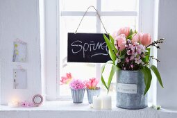 Tulpen und blühende Pfirsichzweige im größeren Gefäß, Tulpen und rosa Hyazinthen in kleinen Zinkgefäßen und Schierertafel am Fenster