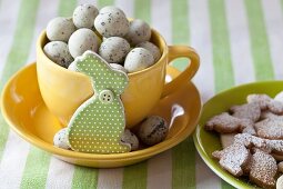 Yellow cup of quail's eggs with rabbit figure and plate of Easter biscuits