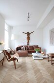 Wohnraum in Braun und Weiß mit lebensgrossem Kruzifix über Ledersofa; Designerstuhl im Fiftiesstil mit Kuhfellbelag