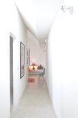Narrow, white corridor with view of classic 50s chair and lit red table lamp in adjoining room