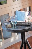 Drinking glasses next to open book on round bistro table in front of glass-fronted cabinet