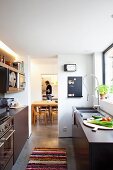 Designer-Einbauküche mit glatten, dunklen Fronten und professioneller Brausenarmatur; Blick auf angrenzendes Esszimmer und Mann im Hintergrund
