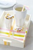 Beaker, drinking straws and toffees on tray decorated with washi tape