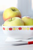 Three apples in china bowl decorated with tape patterned with stylised apples