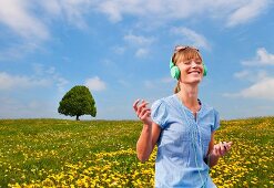 Woman listening to music through earphones in a meadow of dandelions