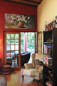 Ohrensessel und Bücherregal vor offener Terrassentür; modernes Stillleben mit Kalla (Illustration) auf roter Wand