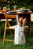 Bag of baguettes hanging on chair back in front of set table in garden