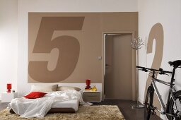 Modern bedroom with bed on floor and parked bicycle leaning on wall painted with large numbers