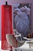 Hängelampe mit Schirm aus roten Fäden und moderner Drehstuhl vor violetter Wand mit Wandbehang