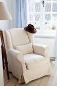 Dark hat on elegant white reading chair next to window