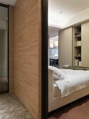 Raumteiler aus Holz vor Bett und Blick auf Einbauschrank