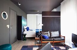 Offener Wohnraum mit grau getönten Wänden und Sitzbank an Raumteiler vor Schlafbereich