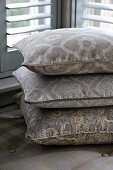 Stack of patterned cushions in bay window with Venetian blinds