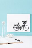 Bicycle motif made from pins and thread on white background on light blue wall