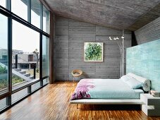 Bett vor bemalter Wand im Schlafzimmer mit Sichtbetonwänden und Fensterfront