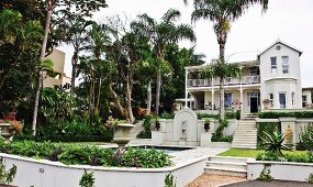 Gartenanlage mit Palmen am Pool und Treppen vor weißem Wohnhaus im Kolonialstil