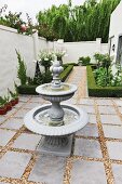 Tiered, antique-style fountain in narrow courtyard with geometric beds
