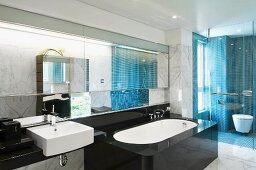 Marmorverkleidetes Designerbad mit schwarz ummantelter Wanne und WC hinter Glasabtrennung