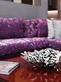 White spheres with black patterns in bowl with flower motif and purple patterned, classic modern sofa in blurred background