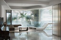 Designer Wohnraum mit Couchtisch im Fiftiesstil auf spiegelndem Steinboden vor Glasfassade mit transparentem Flächenvorhang