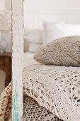 Knitted cushion and crocheted throw in natural-coloured yarns next to wooden post of old bedstead