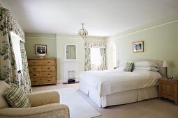 Double bed with upholstered headboard, rustic wooden cabinets and floral curtains with pelmets in spacious, country-house bedroom