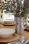 Festively set table with bouquet of dried flowers in decorative blue and white ceramic jug and white soup bowls on basketwork table mats