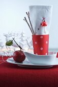 Red and white napkin in red beaker with white polka dots in white bowl on red felt cloth