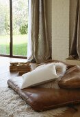 Leather pad, cushions and flokati rug on wooden floor in front of terrace window