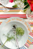 Teller mit Blumendeko und Dessertbesteck auf bunt gestreiftem Tischläufer