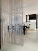 Curved glass pane with string curtain in front of a dining area in a modern living room with white floor tiles