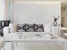 Postmoderner Couchtisch vor Sofa mit Kissen an weiss getöntem Raumteiler mit indirekter Beleuchtung