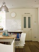 White, modern chair at rustic kitchen table in front of half-height shelving unit against tiled wall in rustic, traditional setting