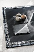 Three pebbles on slate coaster and black place mat with patterned edge