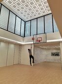 Sportlicher Mann in modernem Raum mit Basketballkorb an Wand