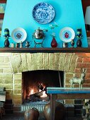 Brick open fireplace with antique silver jugs on mantelpiece and china plates with pictures of beetles on chimneybreast painted light blue