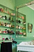 Toiletries on glass shelves in niche next to framed mirror in green bathroom