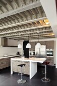 Moderne Designerküche mit grauen Holzfronten unter einer auffälligen, schweren Rippendeckenkonstruktion aus Stahl und Holz