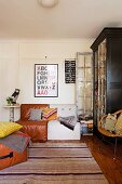 Framed ABC poster above 70s cushion chairs and striped, woven rug in front of large, vintage display cabinet