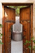 Blick durch geöffnete Holztür auf gefliestem Standwaschbecken im Innenhof