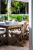 Garden porch with vintage wooden furniture in sunlight; in the background a white garden fence with a hedge